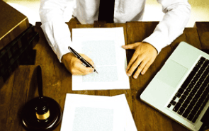 perosna escribiendo en un documento y lapto en mesa